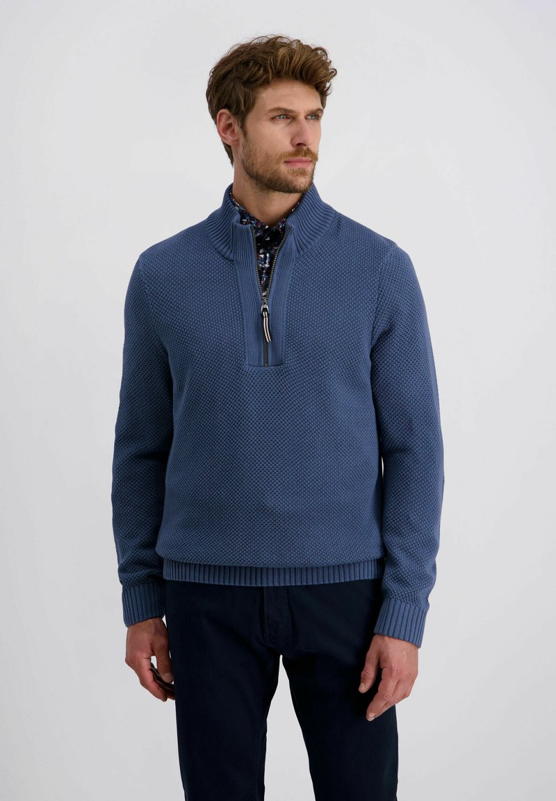 Blauer gestrickter Pullover mit einem halben Reißverschluss-Kragen, strukturiertem Muster, einfarbigen Rippbündchen und Saum, kombiniert mit einem gemusterten Hemd darunter.