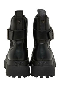 Schwarze vegane Lederstiefeletten mit einer klobigen Sohle, verstellbaren Riemendetails und einem Zugtab hinten. Mit strukturierten und glatten Oberflächen.