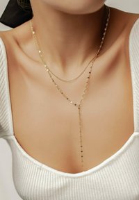 Goldschichtige Halskette mit zarten Ketten, von denen eine kleine goldene hexagonale Akzente aufweist und in der Mitte einen längeren Anhänger hat.