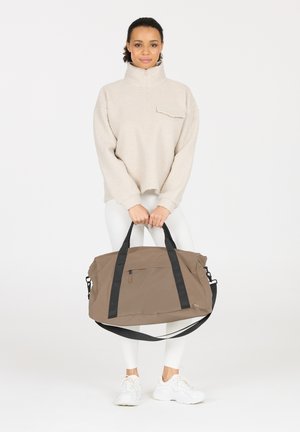 Sac de sport marron avec des sangles noires, présentant une surface texturée, une poche zippée sur le devant et une bandoulière détachable.