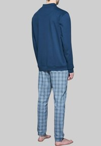 Felpa navy con collo alto, abbinata a pantaloni da pigiama a quadretti blu chiaro e bianchi. Tessuto liscio, vestibilità rilassata, dettagli di cucitura visibili.