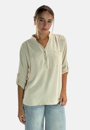 Camicia button-up beige chiaro con scollo a V e una tasca sul petto. Presenta maniche arrotolate e un tessuto morbido e texturizzato.