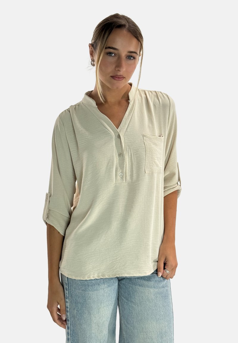 Jasnobeżowa koszula na guziki z dekoltem w serek i jedną kieszonką na piersi. Posiada podwinięte rękawy oraz miękką, teksturowaną tkaninę.