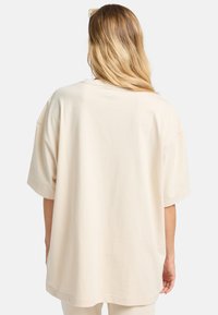 Krème oversized t-shirt med korte ærmer, lavet af blødt bomuld. Har en afslappet pasform og glat tekstur. Minimalistisk design uden synlige mønstre.