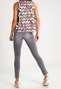 Blusa floreale rosa chiaro con scollo arricciato, abbinata a jeans skinny grigi con dettagli in zip alle caviglie, indossata con sneakers beige.