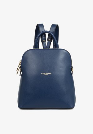 Blue leather backpack with a textured surface, rounded shape, dual shoulder straps, top handle, and a gold logo accent on the front.