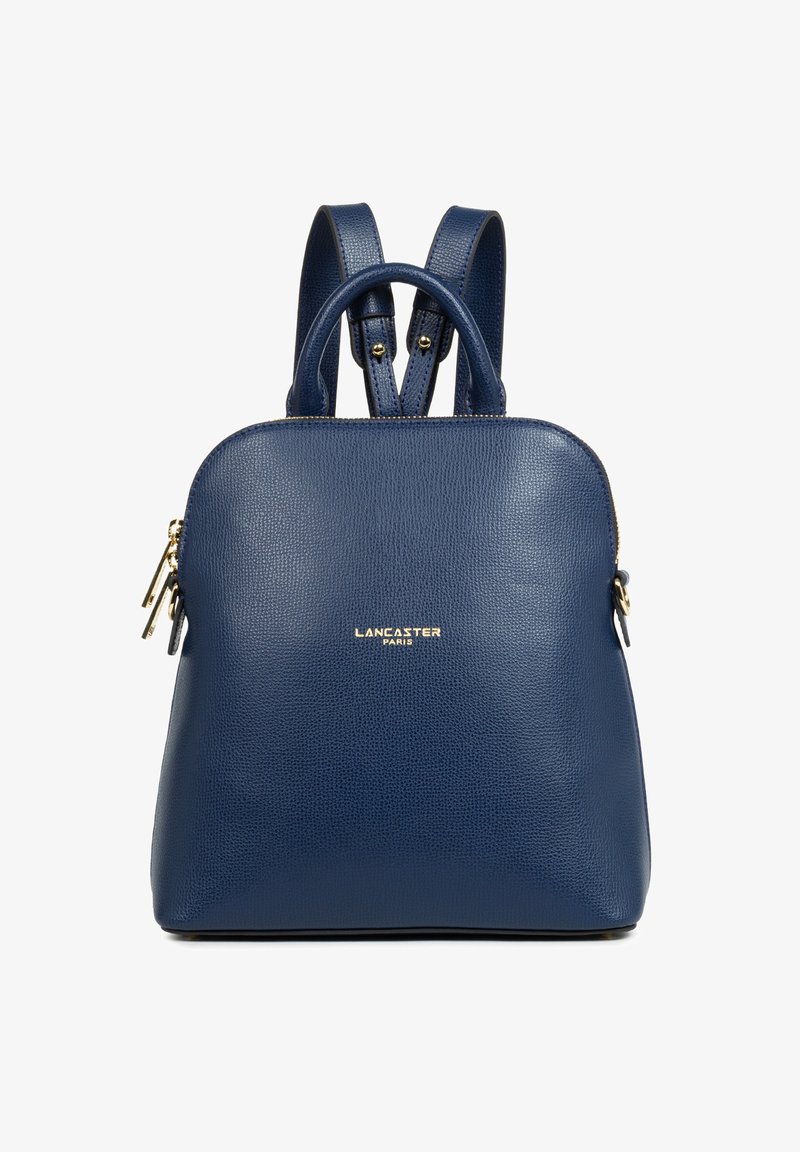 Zaino in pelle blu con superficie testurizzata, forma arrotondata, doppie spalline, manico superiore e un accento logo dorato sul davanti.