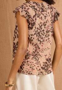 Sheer pink blouse with a leopard print pattern in brown and gold accents; features ruffled sleeves and a rounded collar.