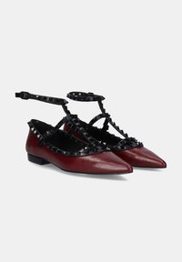 Bailarinas rojas de cuero con correas negras con tachuelas. Diseño de punta afilada, tacón bajo cuadrado y correas de tobillo entrelazadas.