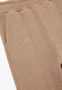 Beige strikkede bukser med en tekstureret finish, der har en elastisk talje og to sidelommer. Designet inkluderer plisserede detaljer.