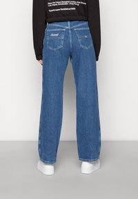 Jeans de mezclilla de pierna ancha en azul claro con dobladillo sin rematar y dos bolsillos traseros. Los jeans cuentan con un logo cosido encima del bolsillo derecho.