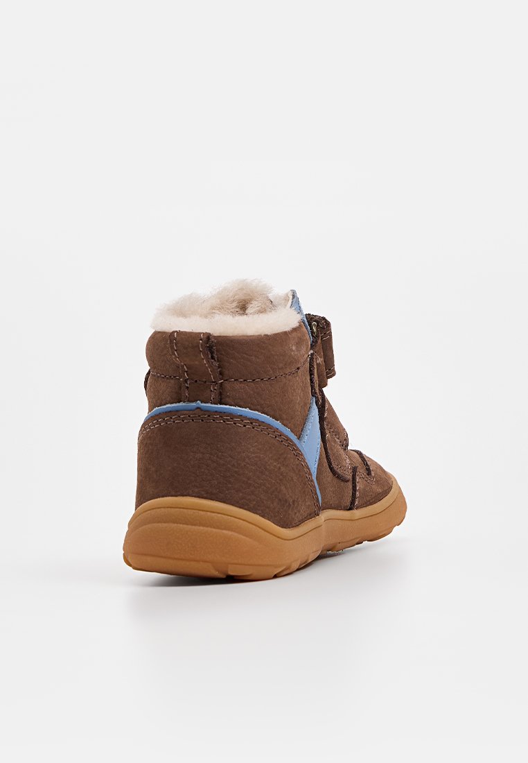 Bottine en daim marron avec une touche de bleu, doublée en fourrure et dotée d'une sangle Velcro. La semelle est flexible avec une adhérence texturée.