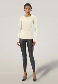 Cremfarbendes, geripptes Langarmoberteil, kombiniert mit figurbetonenden, schwarzen Lederleggings und schwarzen High Heels, die eine elegante, moderne Silhouette schaffen.
