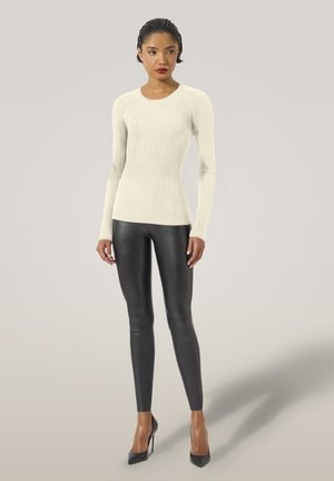 Krämfärgad ribbad långärmad topp i kombination med kroppsnära svarta läderleggings och svarta högklackade skor, vilket skapar en slank och modern silhuett.
