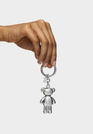 Silver teddy bear keychain held by a hand, featuring a smooth finish, round ears, and visible facial details. Attached to a circular metal ring.