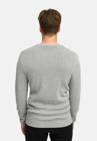 Szary, teksturowany sweter z okrągłym dekoltem i długimi rękawami. Zawiera diagonalne prążkowane wzory. Noszony z ciemnymi spodniami.