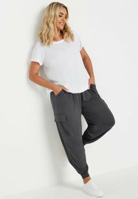 Grå joggare med sidfickor, avsmalnande anklar och elastisk midja, i kombination med en vit t-shirt. Slät textur, avslappnad passform.