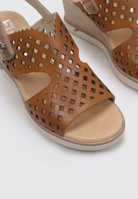 Sandalias de cuña de cuero marrón con diseño de rejilla calada, forro beige y suela de goma ligera, que cuentan con correa para el tobillo ajustable.