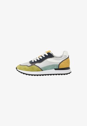 La chaussure présente un design à lacets, utilisant des matériaux en maille et en daim, dans des couleurs jaune, vert, marine et blanc. Semelle noire épaisse avec un motif texturé.