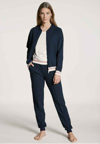 Navyblauwe trainingsset met een bomberjack en taps toelopende broeken, voorzien van gestreepte boorden en een crèmekleurig T-shirt eronder.
