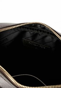 Interior de bolso de cuero marrón texturizado con forro negro, cremallera dorada y una pequeña etiqueta de la marca visible en el lateral.