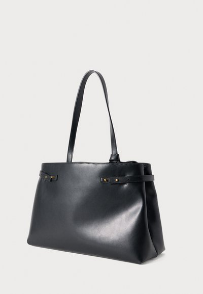 Μαύρη τσάντα tote από δέρμα με ομαλή υφή, ευρύτερη βάση και δύο μακριές λαβές. Διαθέτει λεπτομέρειες σε χρυσό τόνο και μινιμαλιστικό σχεδιασμό.