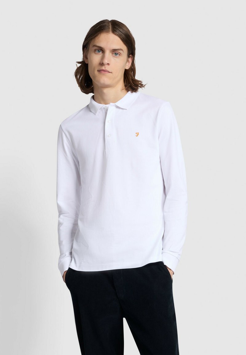 Polo shirt bianco a maniche lunghe con colletto classico, caratterizzato da un piccolo logo arancione sul lato sinistro del petto. Abbinato a pantaloni scuri.