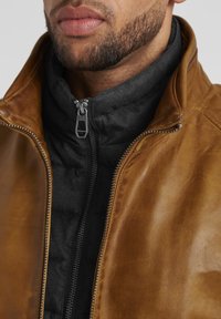 Braune Lederjacke mit einer schwarzen, gesteppten Innenauskleidung, ausgestattet mit einem robusten Reißverschluss und hohem Kragen. Glatte Textur mit kontrastierenden Materialien.