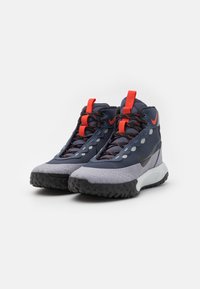 Zilšu un pelēku augstpapēžu sporta apavu pāris ar melnām un sarkanām auklām, sarkanām cilpām, teksturētām melnām zolemn un melnu Nike swoosh logo.