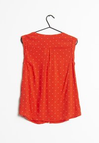 Rode mouwloze top met een ronde halslijn, versierd met witte hartvormige stippen en een geplooide achterkant, hangend aan een zwarte hanger.