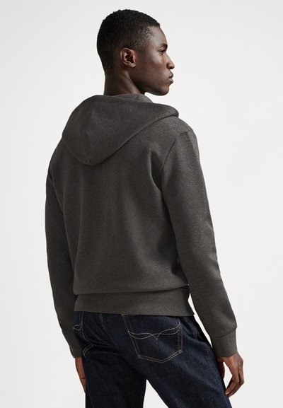 Σκούρο γκρι φούτερ με κουκούλα, με υφή υφάσματος και ριμπ μανσέτες, σε συνδυασμό με σκούρο μπλε τζιν με διακριτικές ραφές.