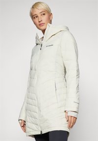 Hvid dunjakke med hætte, med en quiltet design, lynlås foran og logoer. Materialet ser blødt ud med en glat tekstur.