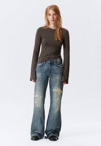 Gestreiftes Langarmoberteil in Braun und Beige, kombiniert mit hellblauen Jeans mit ausgefransten Säumen und abgeriebenen Stellen.