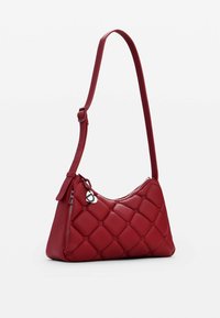 Red leather handbag with a quilted design, a single adjustable strap, zip closure, and a decorative charm. Smooth texture and rounded shape.