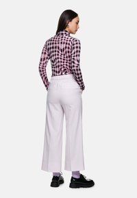 Fitted pink and black checkered long-sleeve top paired with wide white trousers, featuring an elastic waistband and black platform shoes.