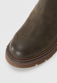 Brown leather ankle boot with a rounded toe, stitched edge, rubber sole, and embossed "TOM TAILOR" detailing along the sole.