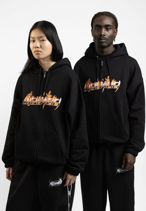 Black zip-up hoodies with an orange flame logo on the chest. The fabric appears soft, with ribbed cuffs and matching black sweatpants featuring a white print.