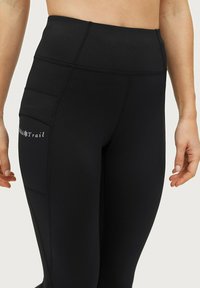 Zwarte hoge taille leggings met een gladde textuur, voorzien van een grote zijzak en contrasterende witte logodetails langs het been.