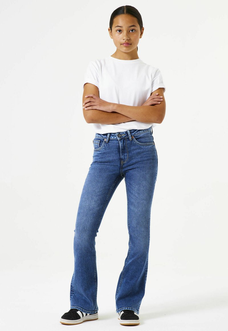 Blue denim flared jeans with light wash, five pockets, and a button closure. Paired with a plain white short-sleeve t-shirt and black sneakers.