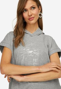 Hoodie gris clair à manches courtes, avec un design graphique blanc représentant un visage et le texte "Moin". Tissu doux avec une coupe décontractée.