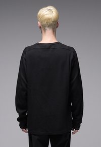 Camisola preta de manga comprida com padrão texturizado em padrão waffle, corte descontraído e decote redondo. Apresenta ombros caídos e punhos canelados.