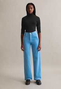 Col roulé noir à manches longues associé à un pantalon en velours côtelé bleu clair, taille haute et jambes larges, ainsi qu'à des chaussures à plateforme noires. Texture lisse partout.