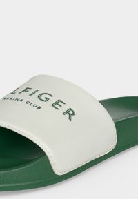 Sandale slide verte avec une bride blanche comportant un texte "Tommy Hilfiger Marina Club" vert foncé.