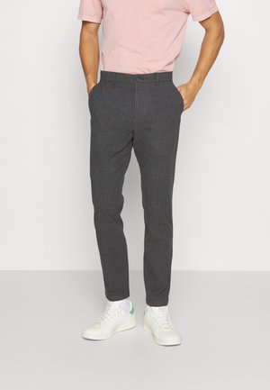 Grårandiga byxor med en figurnära design, med sidofickor och midjeband. Matchas med vita sneakers med gröna detaljer.
