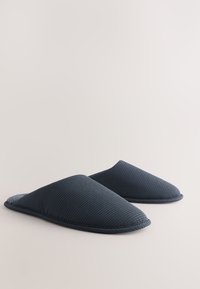 Sötétkék, texturált szövetből készült, zárt orrú, puha béléssel ellátott házicipőpár, egymás mellett elhelyezve, egyszerű világos háttéren.