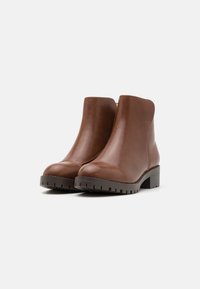 Botines de cuero marrón hasta el tobillo con punta redondeada, cremallera lateral y suela de goma texturizada. Presentan un tacón bajo y un diseño limpio.