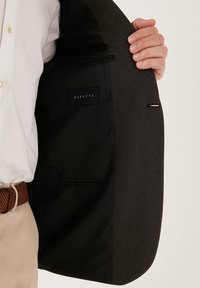Giacca su misura con un esterno grigio scuro testurizzato, fodera nera e etichetta Buratti; presenta una tasca interna singola con finitura liscia.