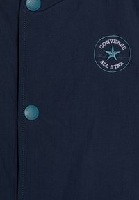 Granatowa koszula zapinana na guziki, wykonana z lekkiego materiału, z haftowanym okrągłym logo przedstawiającym gwiazdę i napisem "Converse All Star".