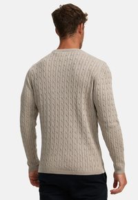 Beige kabelstrikket genser med ribbede mansjetter og kant, som har et teksturert overflate mønster. Klassisk genserdesign med rund hals og lange ermer.