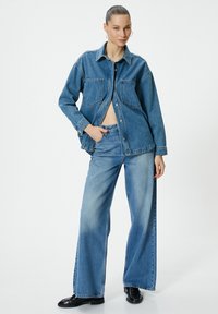 Jeansjacka med två framfickor, bärs över en crop top, ihop med vida jeansbyxor. Ljusblå tvätt med blekta accenter.